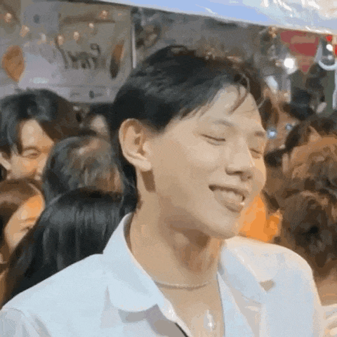 a young man in a white shirt is standing in a crowd of people and smiling .