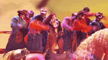 a woman is singing into a microphone while surrounded by cowboys on a pink horse .