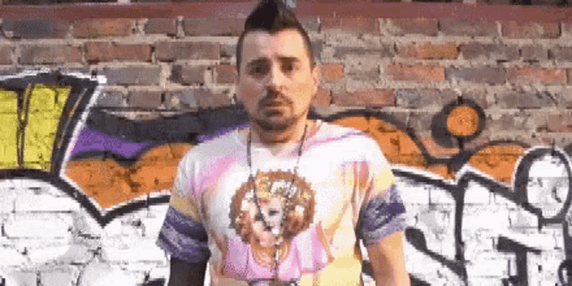 a man is standing in front of a graffiti covered brick wall .