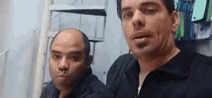 two men are making funny faces in front of a ladder .