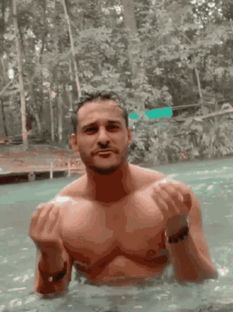 a shirtless man is swimming in a body of water and giving the middle finger