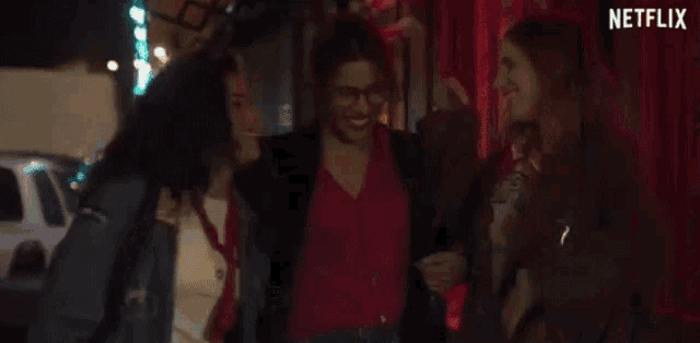 a group of women are hugging each other on a street at night .