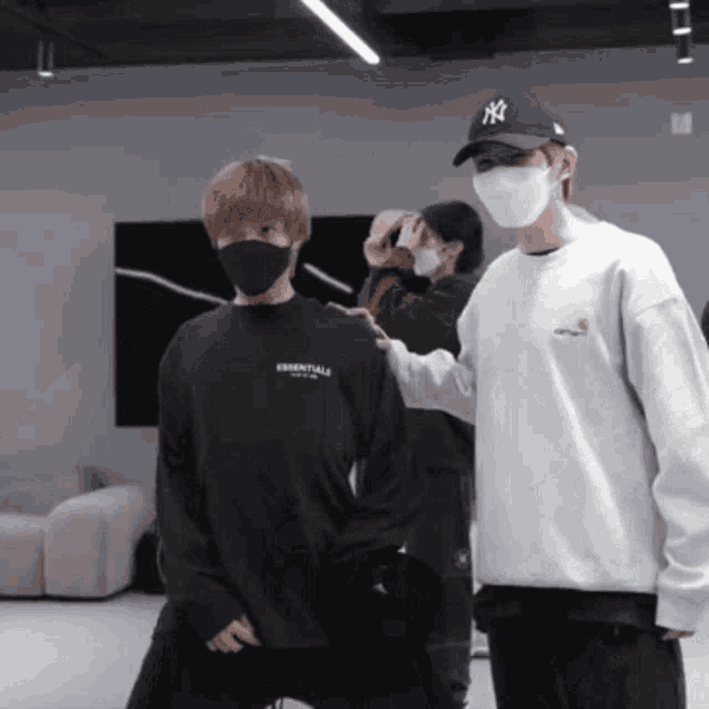 a man wearing a ny hat stands next to a man wearing a black essentials shirt
