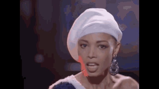 a woman wearing a white hat and earrings is standing in a dark room .