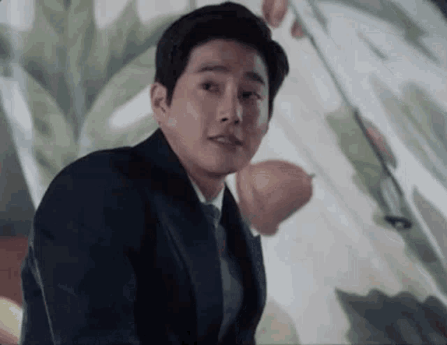 a man in a suit and tie is sitting in front of a painting of flowers .