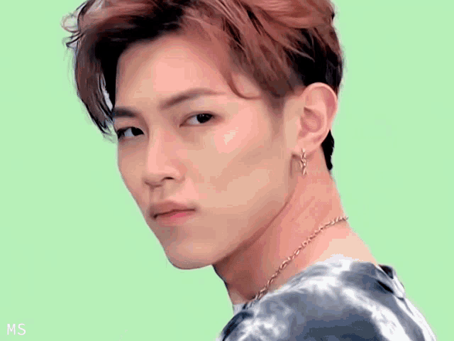 a young man wearing a tie dye shirt and earrings looks over his shoulder at the camera