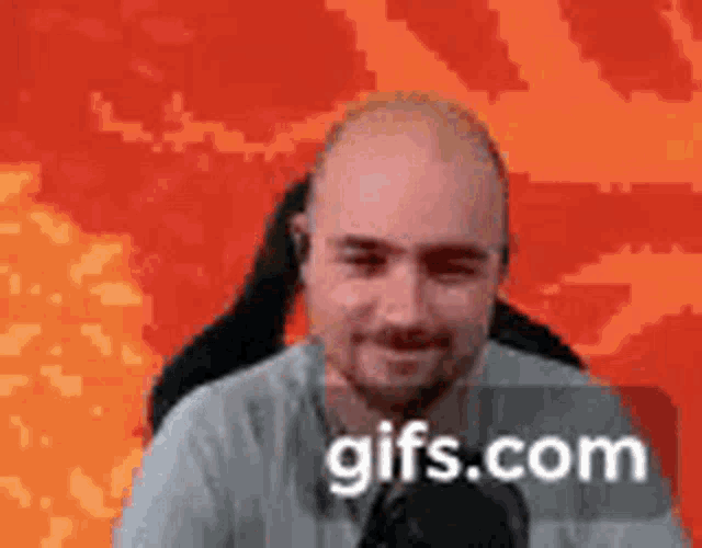 a bald man with a beard is sitting in front of a red background and smiling at the camera .