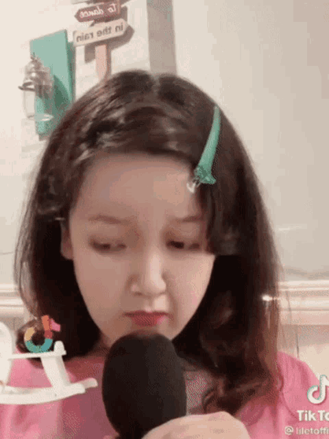 a girl in a pink shirt is holding a microphone in front of her face .