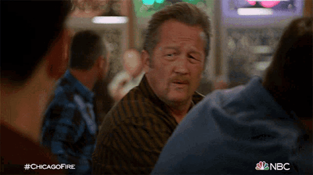 a man in a striped shirt is talking to another man in a bar with #chicagofire written on the bottom right