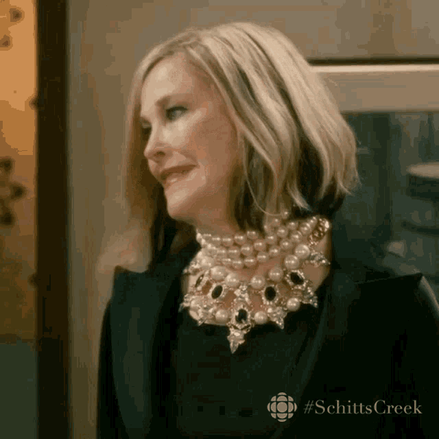 a woman wearing a black jacket and a pearl necklace is smiling .