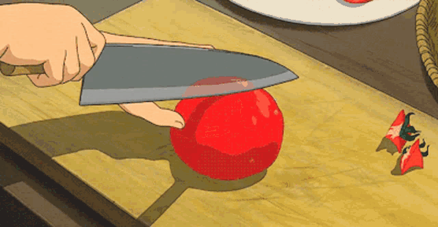 a person is cutting a red tomato on a wooden cutting board