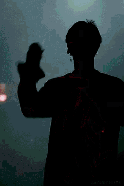 a silhouette of a man in a black shirt is dancing on a stage in the dark .