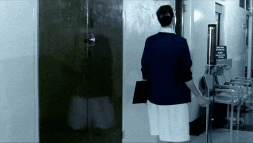 a woman in a blue jacket and white skirt is standing in front of a door with a sign that says no smoking