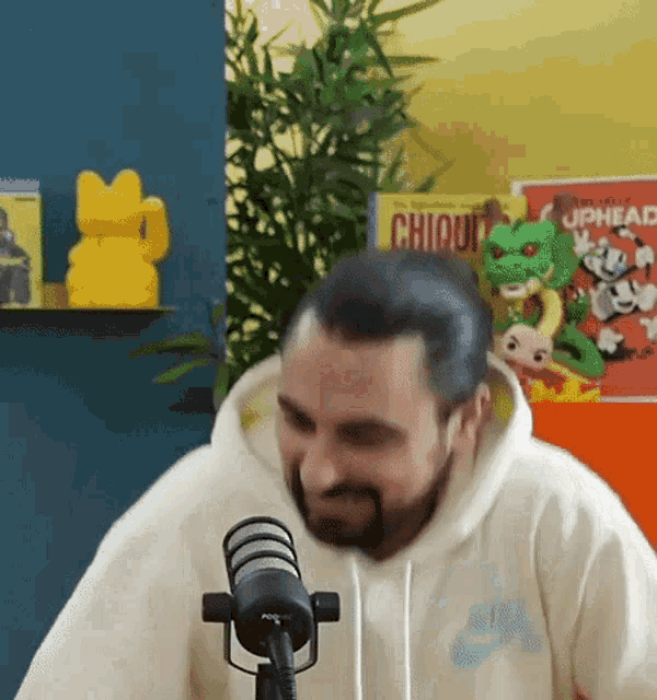 a man with a beard is standing in front of a microphone with a cuphead poster in the background .