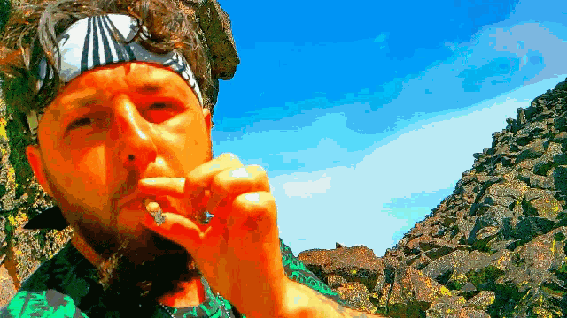 a man wearing a bandana smoking a cigarette in front of a mountain