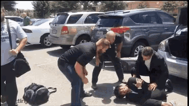 a group of people are standing around a man laying on the ground in a parking lot
