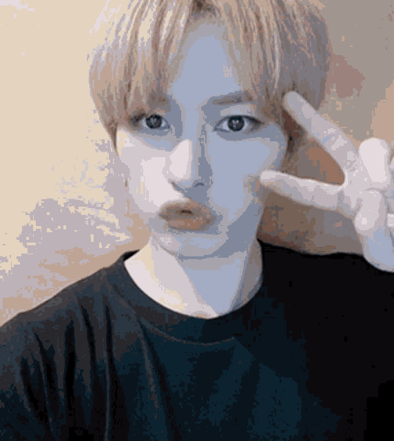 a young man with blonde hair is making a peace sign with his hands .