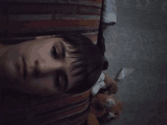 a young man laying on a bed with a stuffed animal in the background