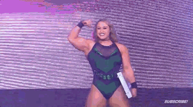 a woman in a green swimsuit is flexing her muscles while holding a trophy .