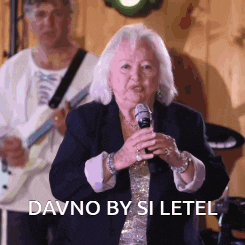an elderly woman singing into a microphone with the words davno by si letel behind her