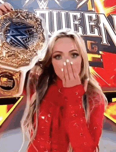 a woman in a red dress is holding a wrestling championship belt and blowing a kiss