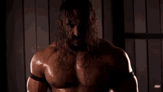 a wrestler with long hair and a beard is standing in a dark room