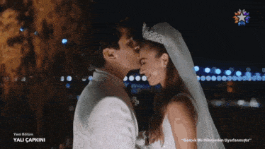 a bride and groom are kissing in front of a sign that says yalı capkini
