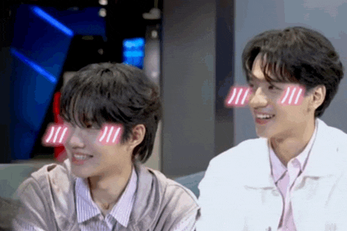 two young men are sitting next to each other and one of them has a sticker on his face that says " i love you " .
