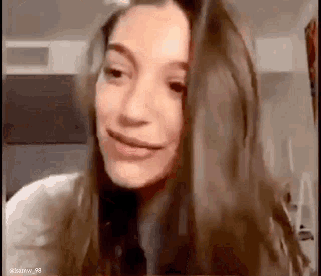 a woman with long brown hair is smiling and looking at the camera in a room .