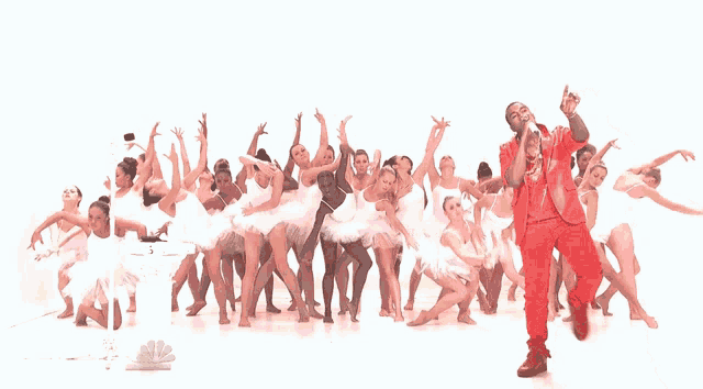 a man in a red suit is singing into a microphone in front of a group of dancers
