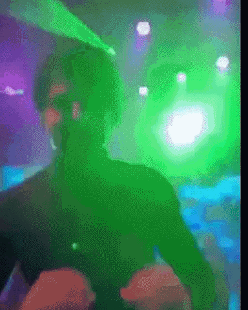 a blurry picture of a man dancing in a dark room with green lights behind him