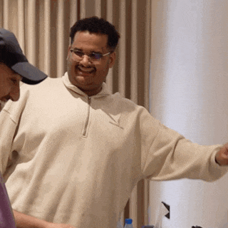 a man wearing glasses and a hat stands next to another man wearing a sweater