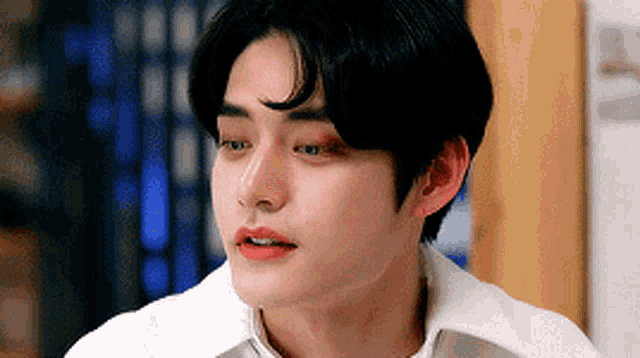 a close up of a young man 's face with his eyes closed and a white shirt on .