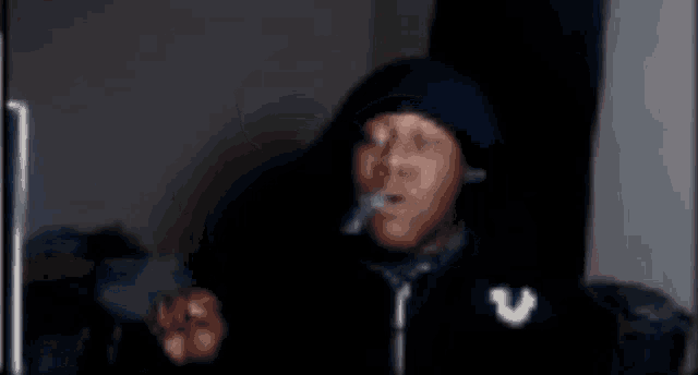 a man in a black hoodie is smoking a cigarette in a dark room