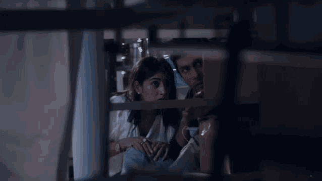 a man and a woman are kissing in a dark room behind a window .