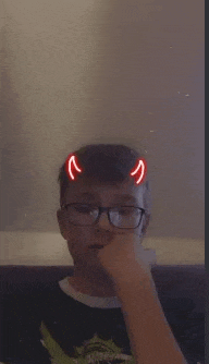 a young boy wearing glasses and devil horns is covering his face with his hand .