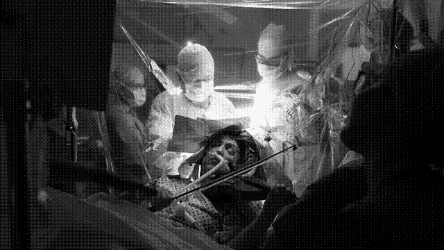 a black and white photo of a person in a hospital bed playing a violin while being operated on .