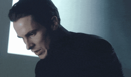 a man in a black turtleneck looks down in a dark room