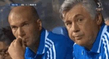 two men in blue shirts are watching a soccer game with the number 3 on the bottom of the screen