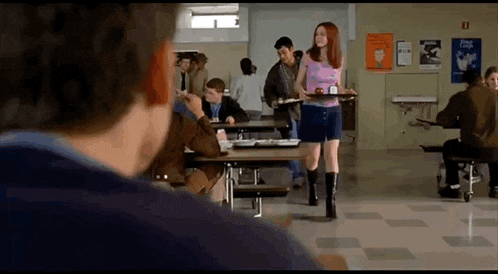 a woman is carrying a tray of food in a cafeteria while a man looks on .
