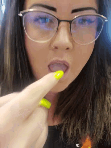 a woman wearing glasses has a yellow nail polish on her finger