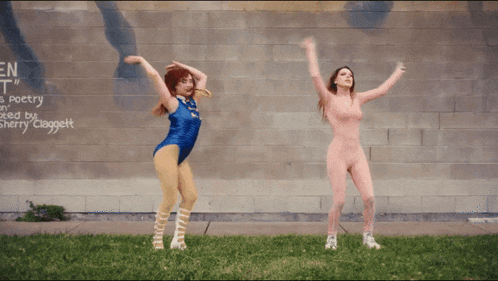 two women are dancing in front of a wall that has the word poetry on it