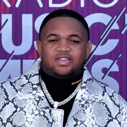 a man wearing a snakeskin jacket is standing in front of a sign that says us