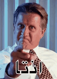 a man in a suit and tie is pointing at the camera with arabic writing on his face