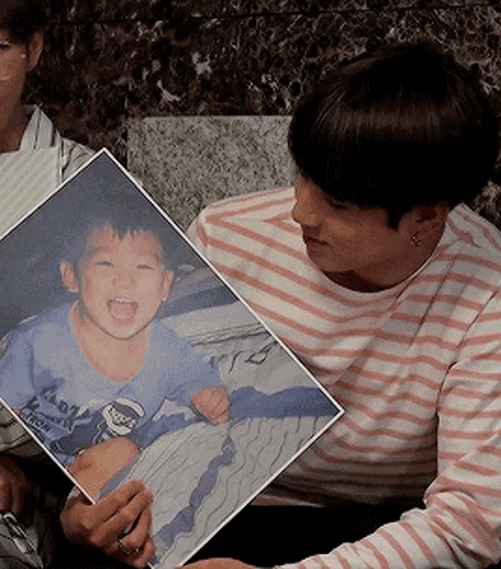 a man in a pink and white striped shirt is holding a picture of a little boy