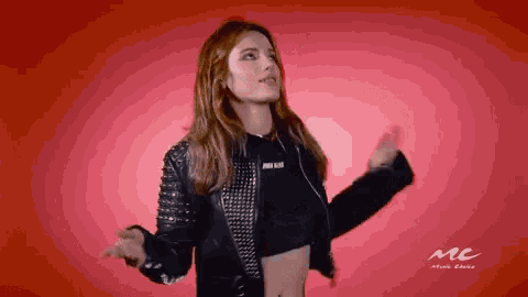 a woman in a crop top and studded leather jacket is dancing in front of a red background that says music choice