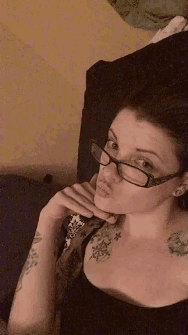 a woman wearing glasses and a black shirt has a tattoo on her shoulder