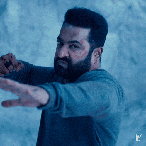 a man with a beard is wearing a blue shirt and pointing