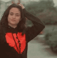 a woman wearing a black hoodie with a red heart on it is holding her hair .