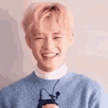 a young man in a blue sweater is smiling while holding a microphone .